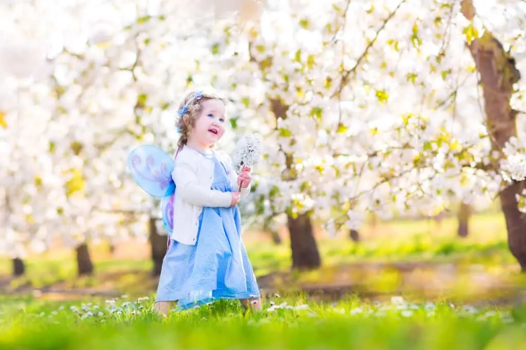 Baby wears fairy-inspired costume in front of blossoming trees.