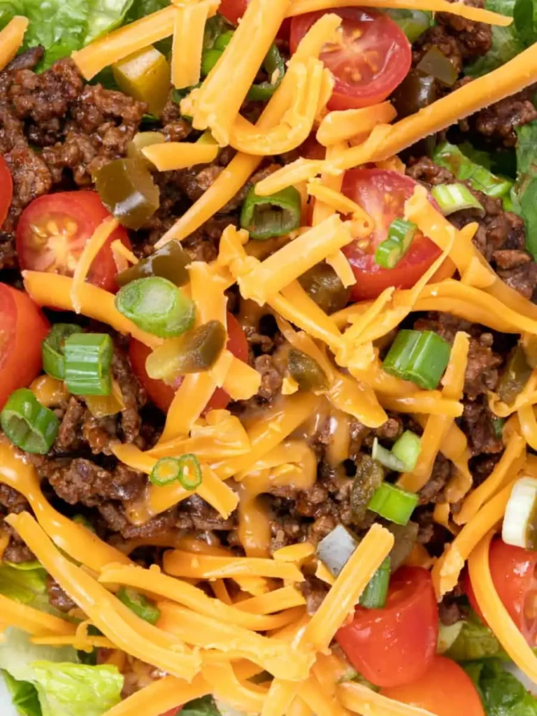 Close-up image of taco salad with ground beef, shredded cheese, green onions, and tomatoes.
