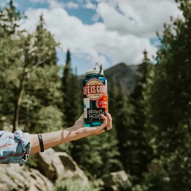 hand holding water bottle outdoors while camping