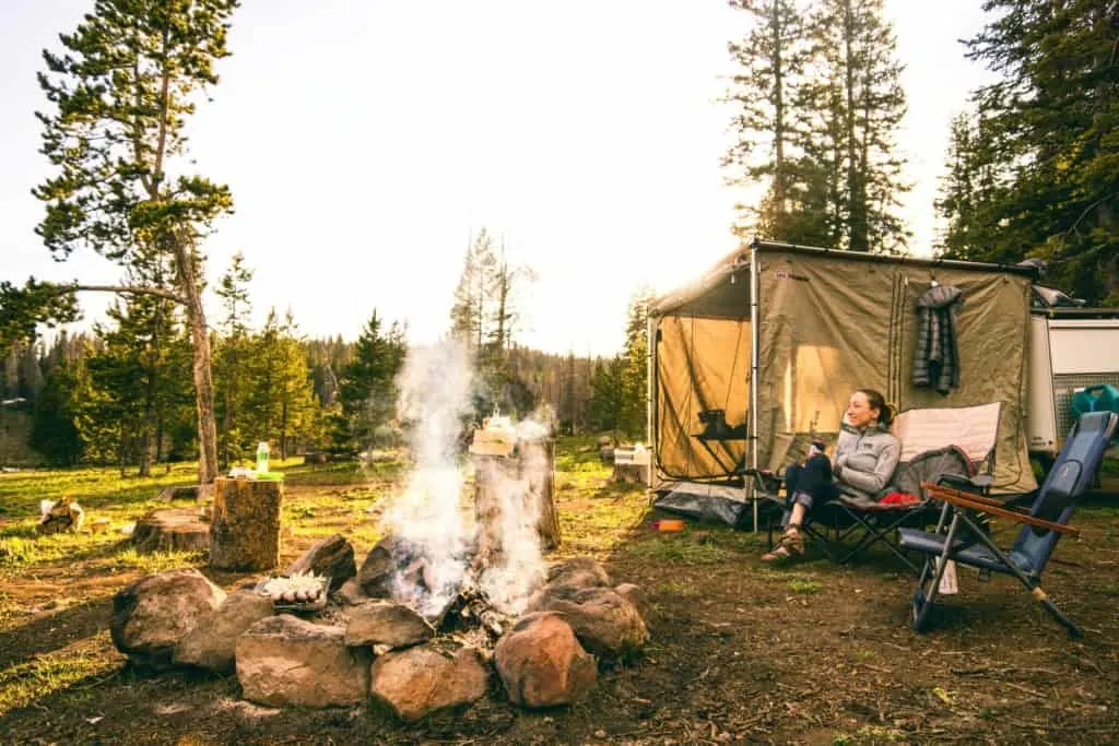 female camper and camping supplies around a campfire