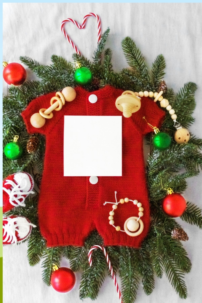 A Christmas baby onesie on a wreath with ornaments.