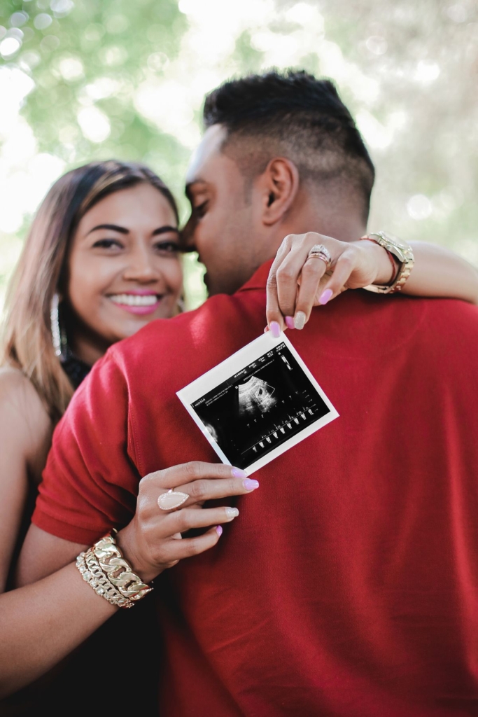 A couple embraces while holding up an ultrasound photo.
