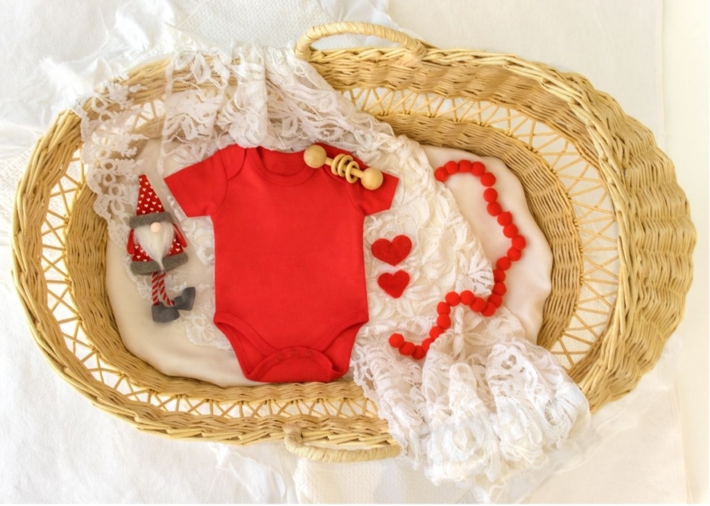Flat lay baby announcement for Christmas using a red onesie and a basket.