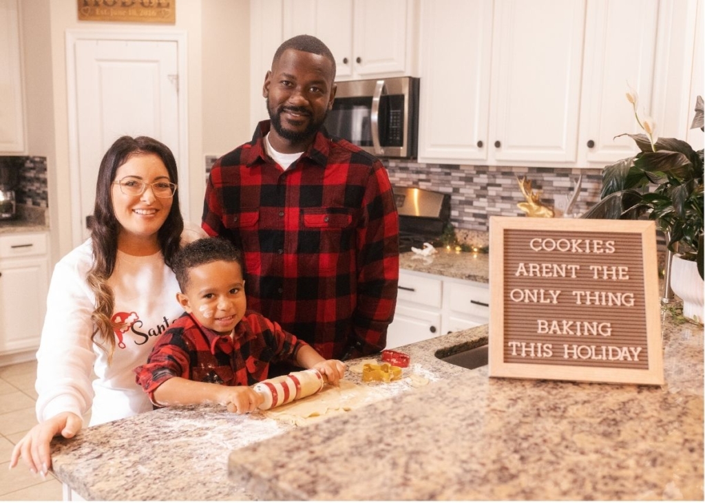A family next to a Christmas pregnancy announcement sign on their kitchen counter.