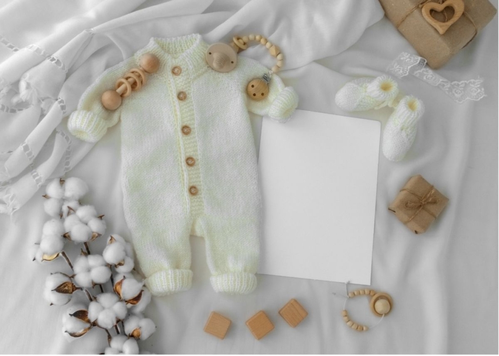 Flat lay baby announcement with a baby onesie and cotton.