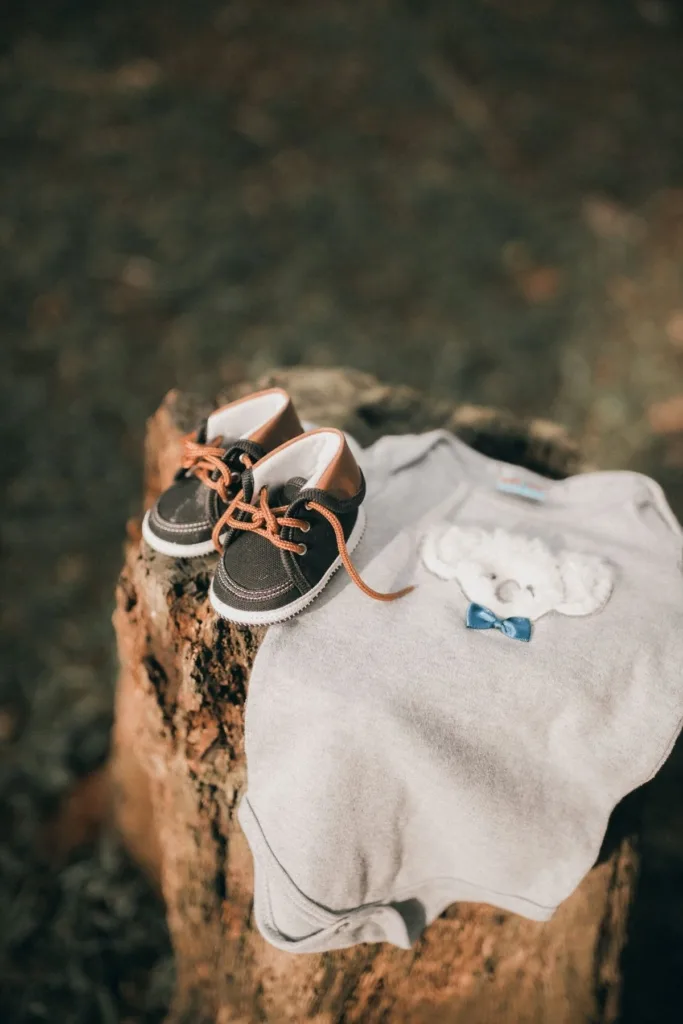 Baby shoes and a onesie on a tree stump outside.