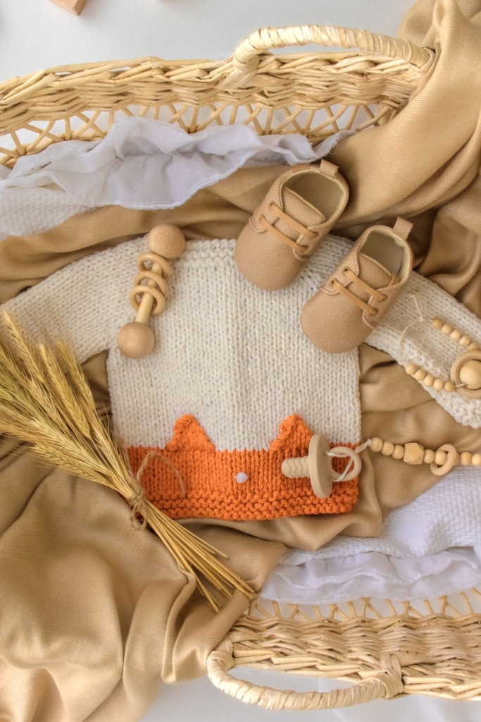 Fall flat lay pregnancy announcement with baby clothes and wooden beads.