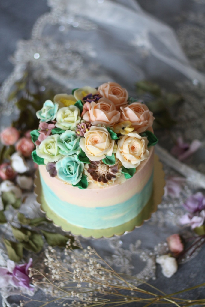 A pink and blue spring cake surrounded by flowers.