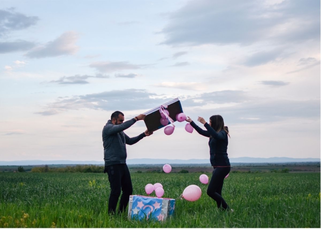 A couple opens a box of pink balloons outside.