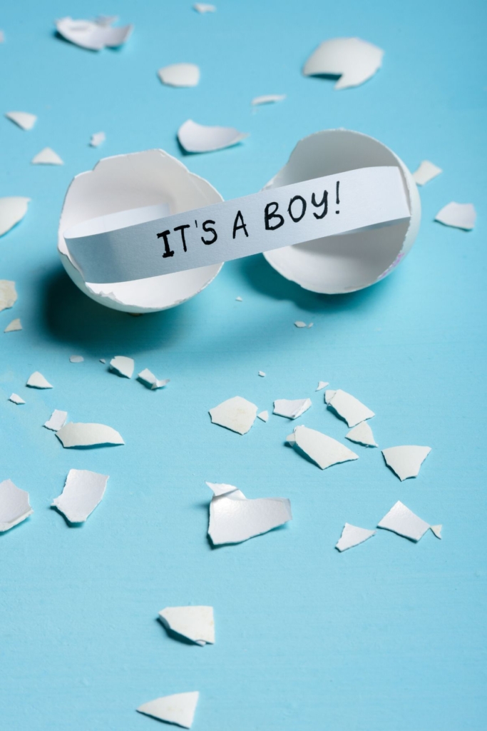 A note that says "it's a boy" popping out of an egg on a blue background.