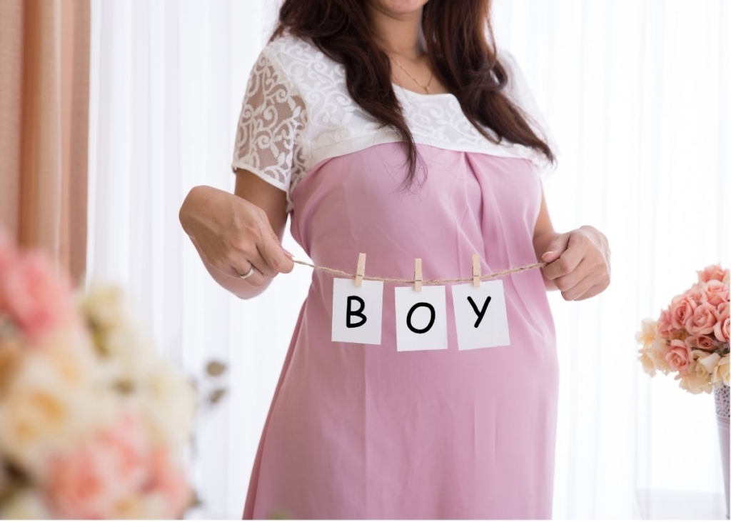 A woman in a spring dress holds a sign that says "boy".