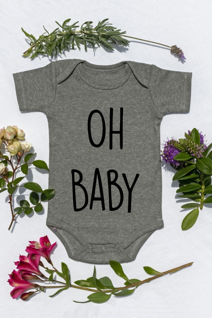 A gray bay onesie with the words "oh baby" in black surrounded by spring flowers.