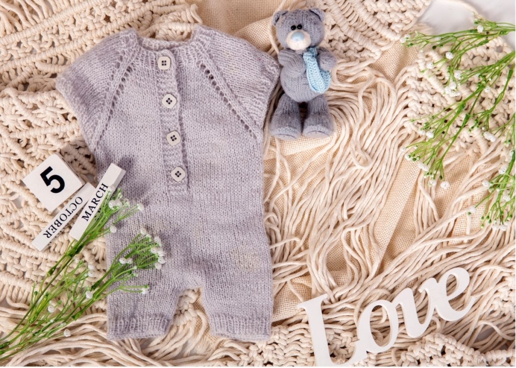 A gray baby onesie on a furry rug surrounded by spring decor.