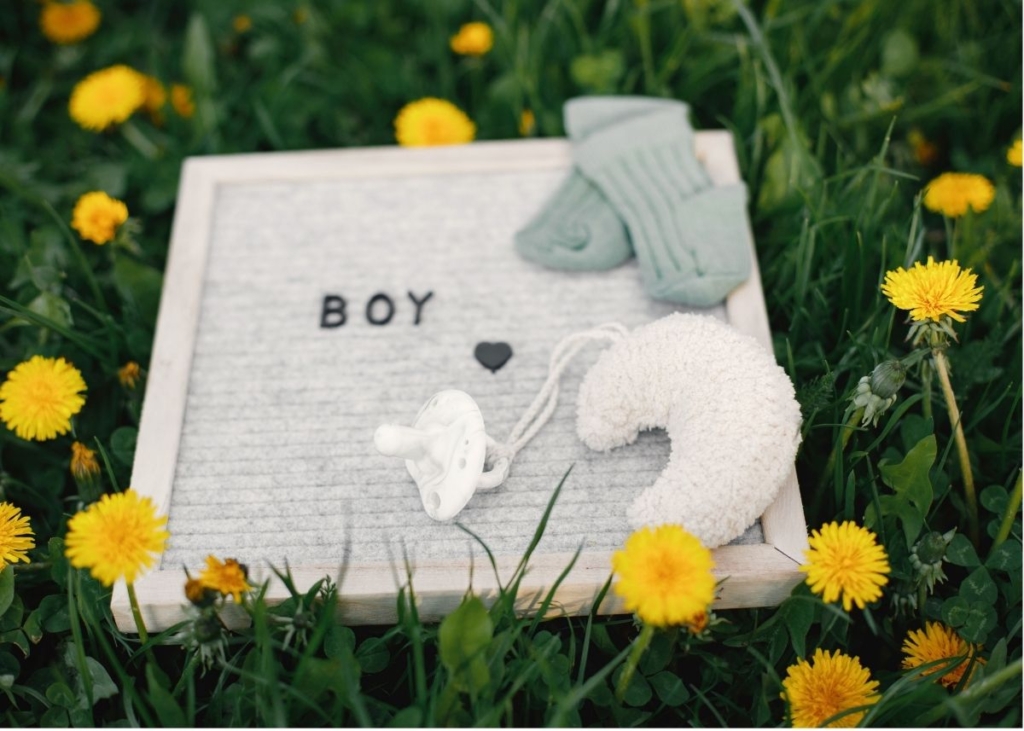 A sign that says "boy" in the grass with baby items.