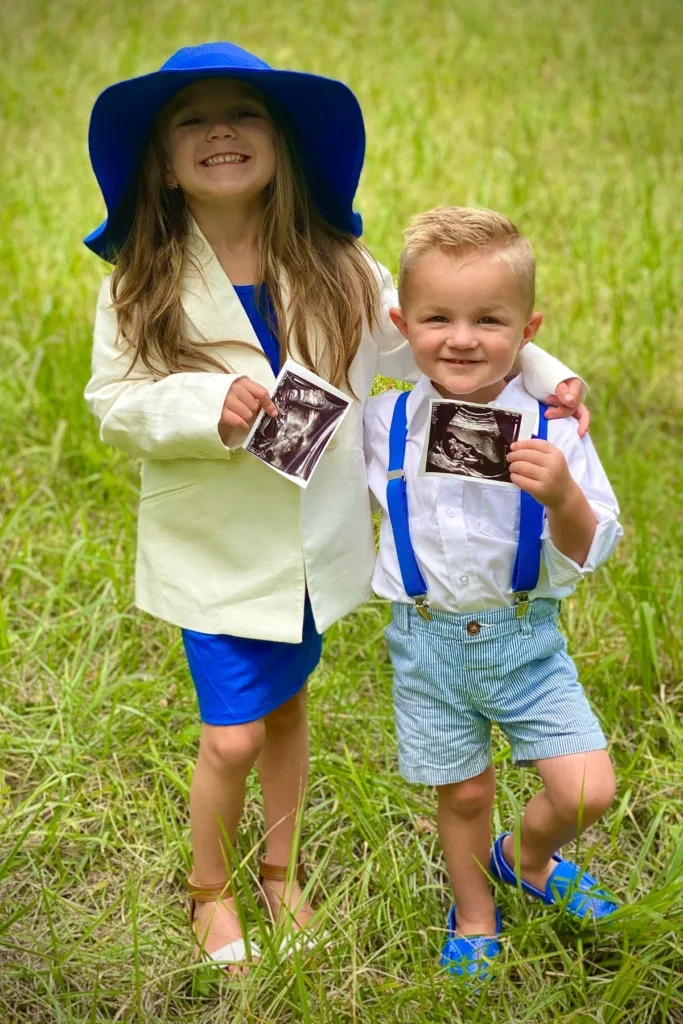 Two children wearing blue hold up ultrasound photos.