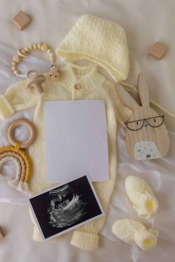 A yellow baby onesie with an ultrasound photo and a wooden bunny.