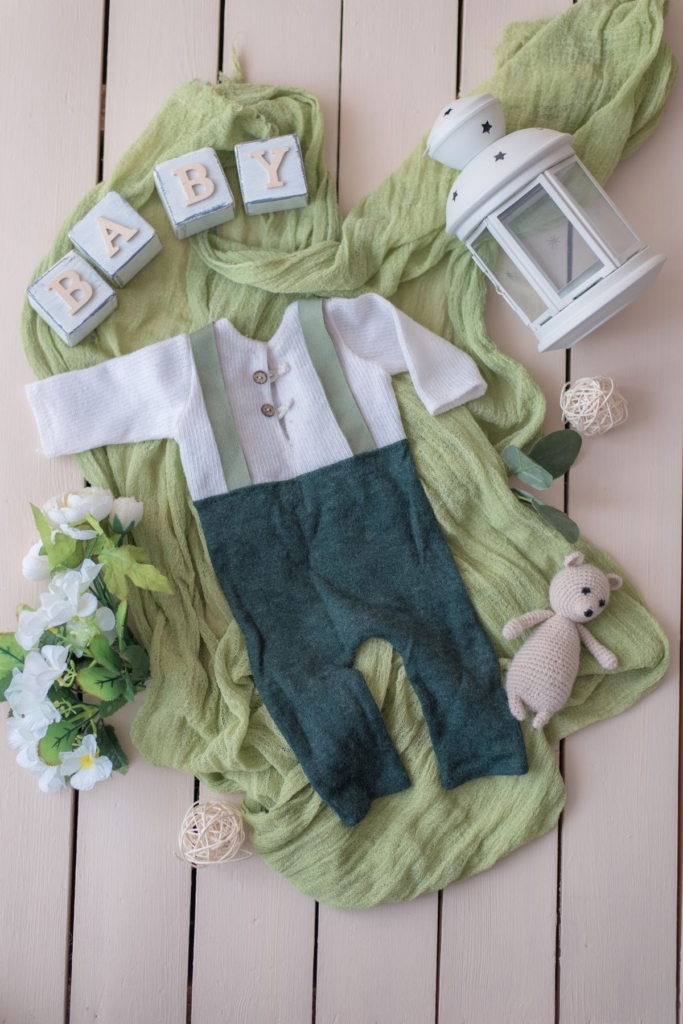 A baby boy suspenders outfit surrounded by spring decorations.