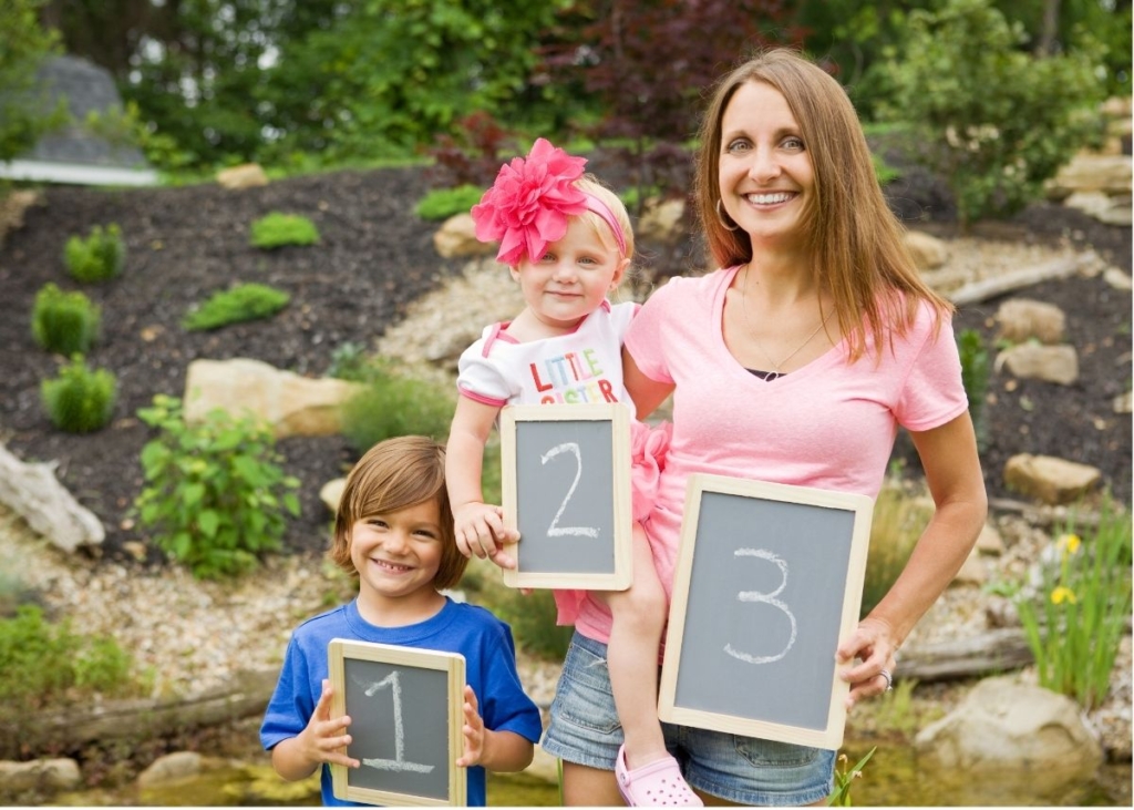 A mom and and kids hold up chalkboard signs with 1, 2 and 3 on them.