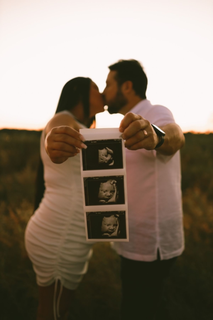 A couple holds up ultrasound phots outside in the sunset.