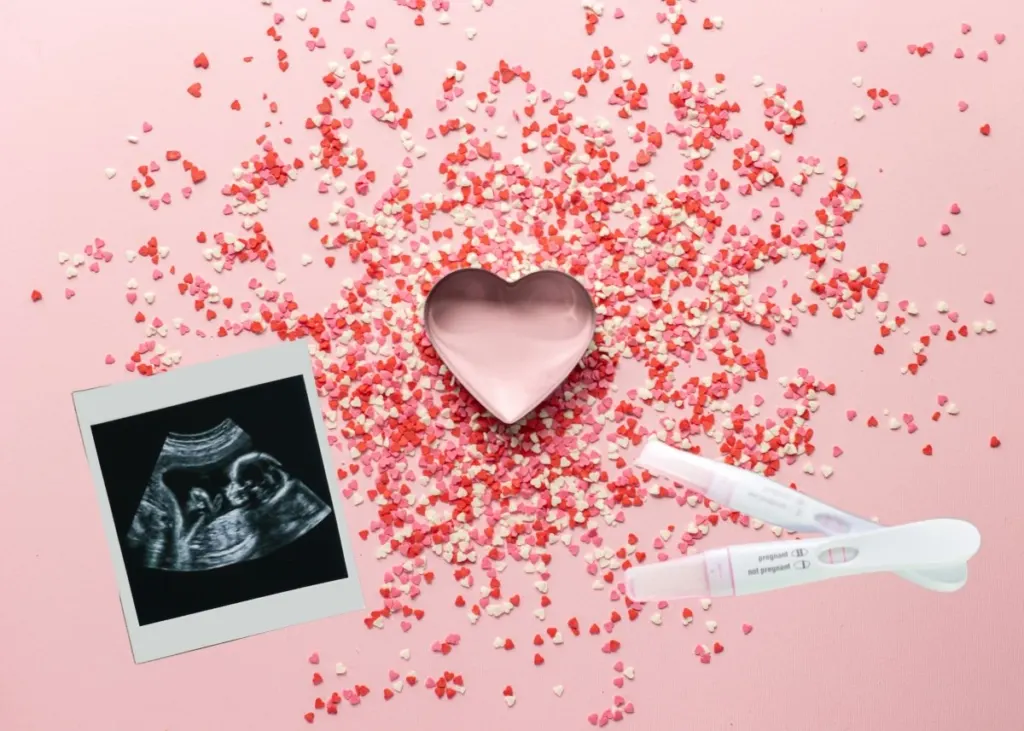 Valentine's Day baby announcement with heart confetti, and ultrasound photo, and pregnancy tests.
