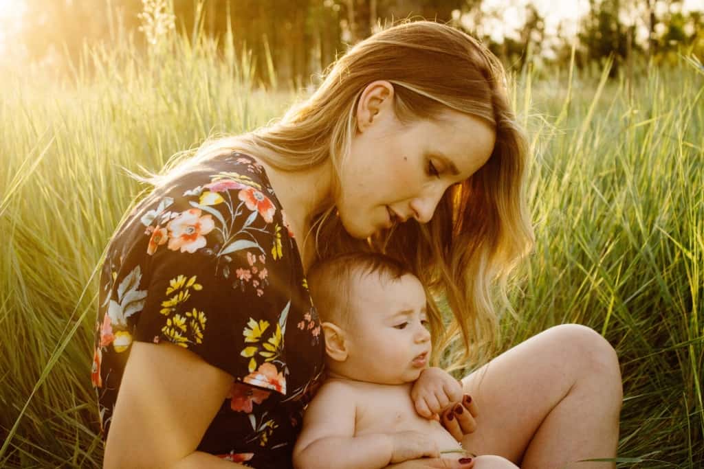 Mother sits with baby girl in tall grass.