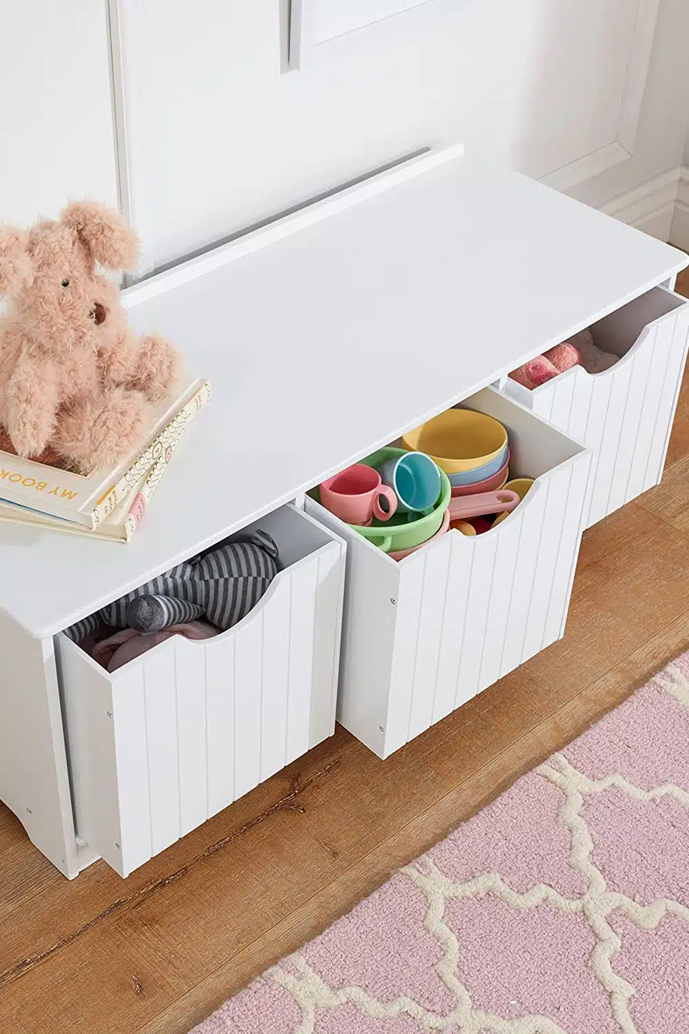 Toy storage bench with drawers slightly pulled out and a teddy bear on top.