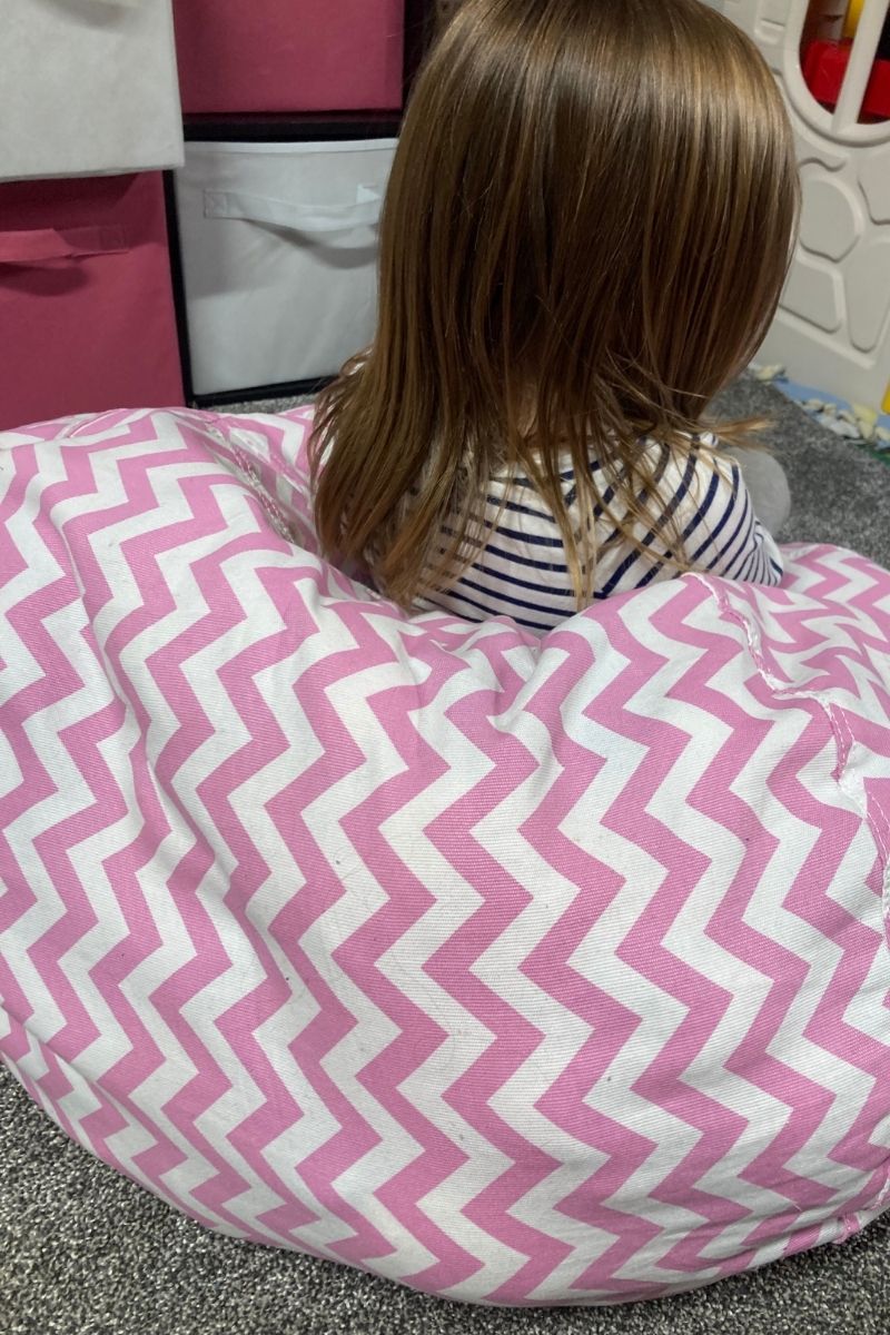 A girl sitting on a bean bag with pink and white chevron stripes.