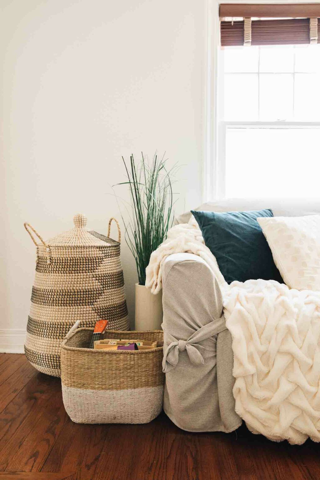 A woven storage basket and hamper beside a couch with toys inside.