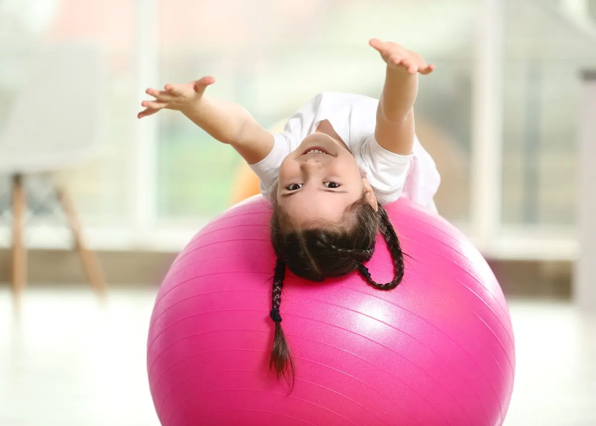 A little girl reaching backward over a pink yoga ball.