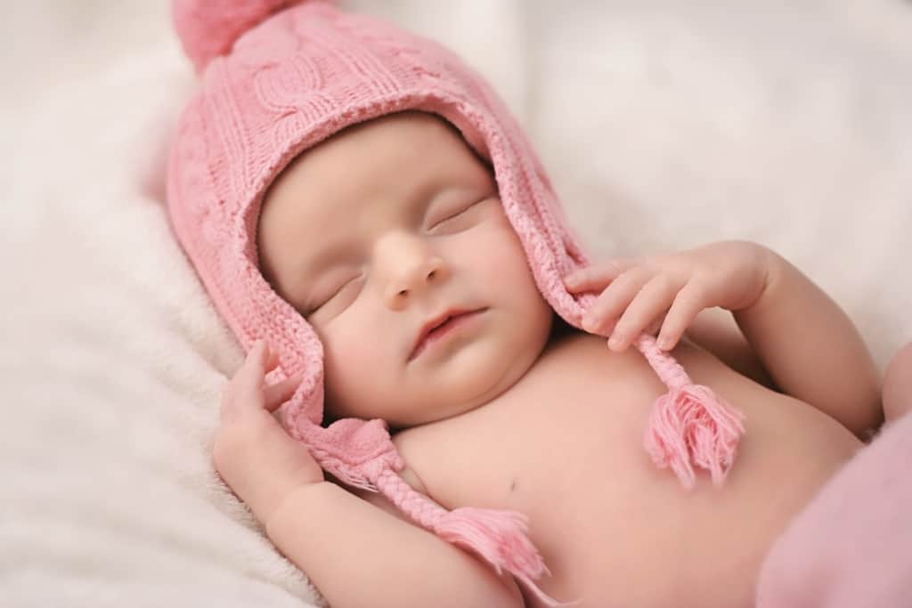 Baby girl sleeps in pink beanie.