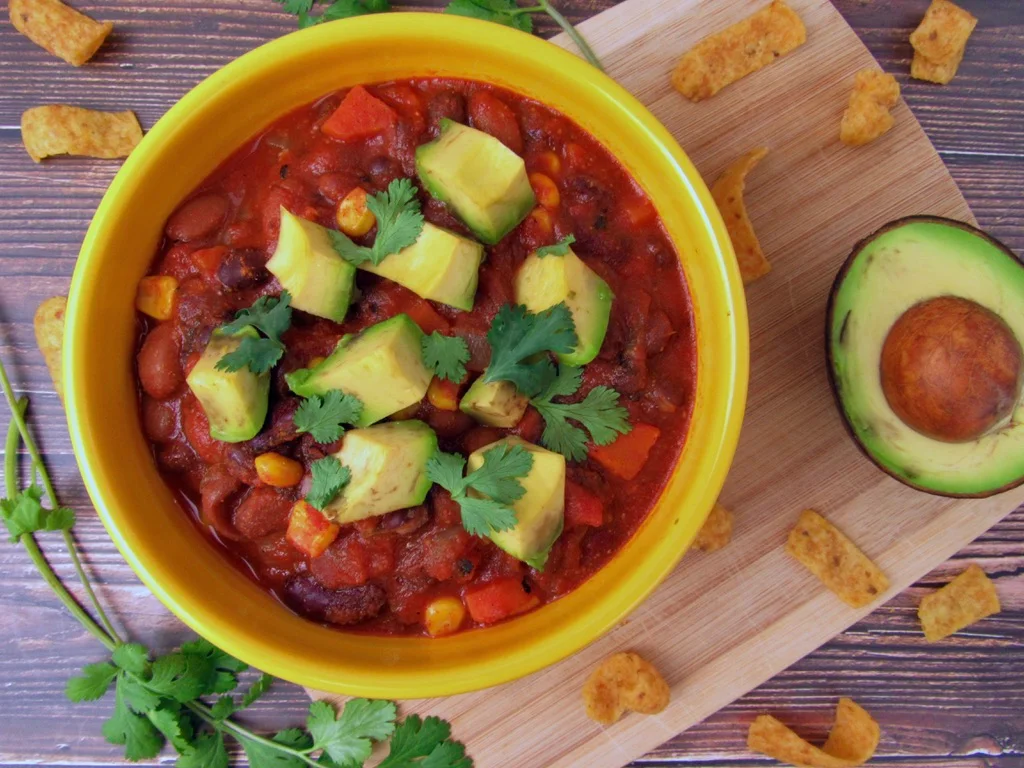 Veggie chili in a yellow bowl with avocado cubes and cilantro on top.