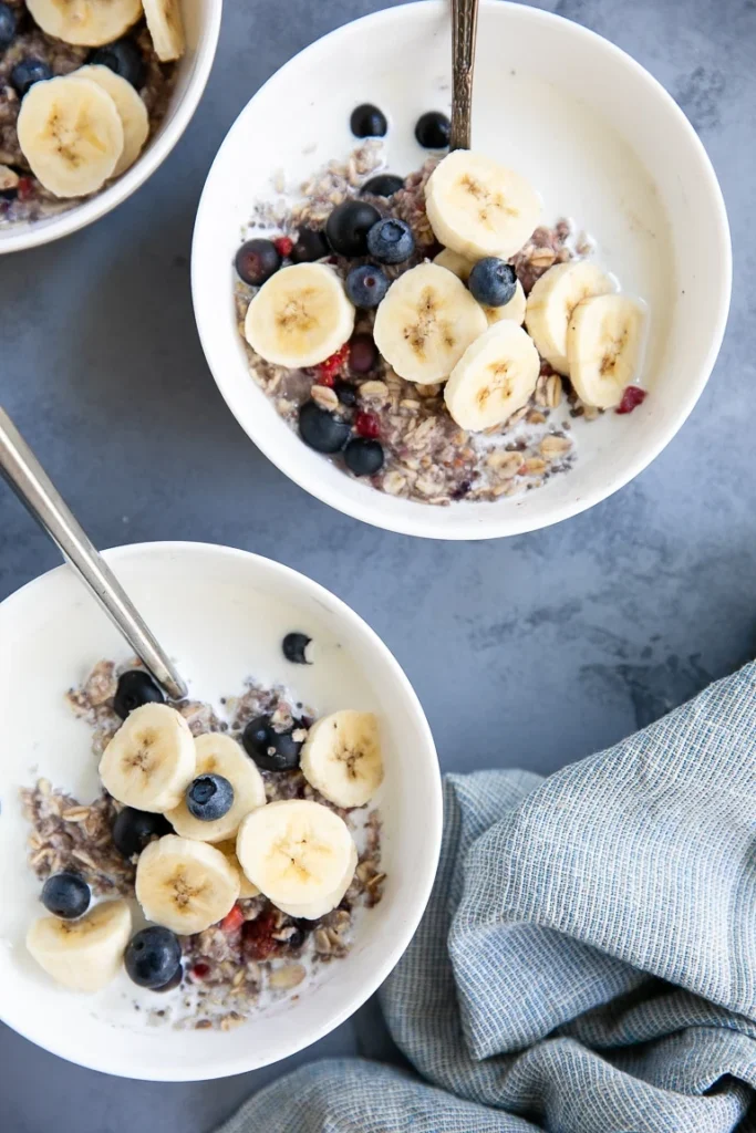 Oatmeal in two bowls with berries and bananas on top.