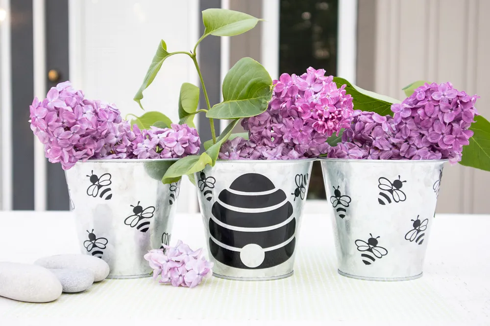 Cricut decorated summer plannters with purple flowers inside.