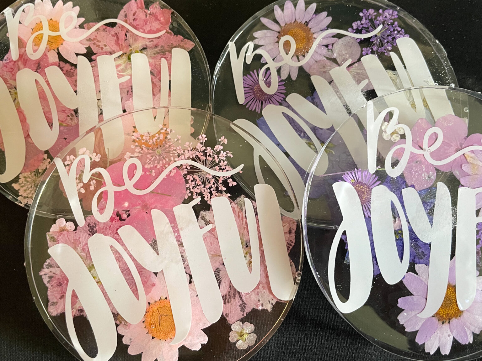 Homemade resin coasters with positive words and flowers.