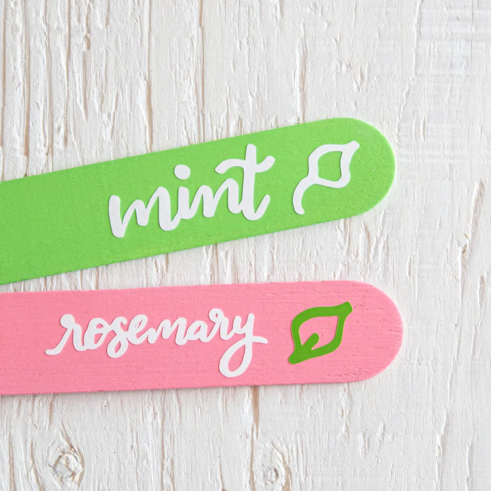 Pink and green herb markers on a white wood background.