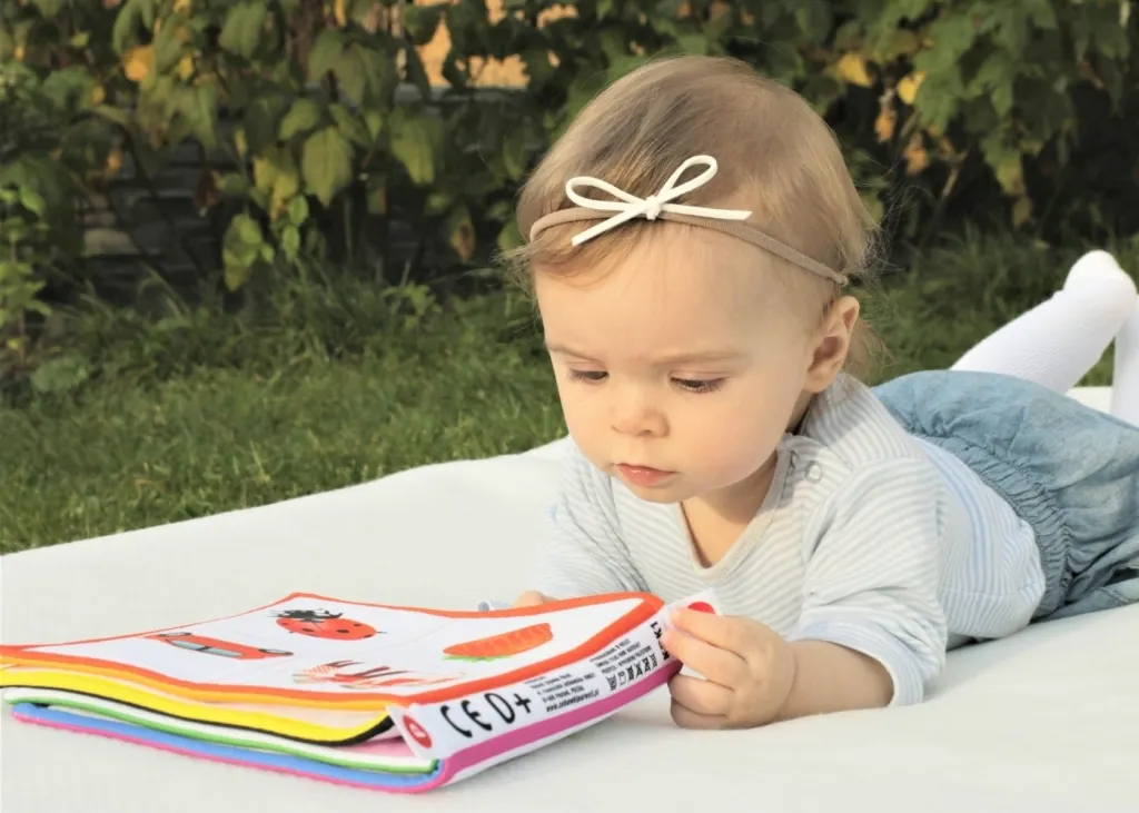 1-year-old girl reads book on blanket.