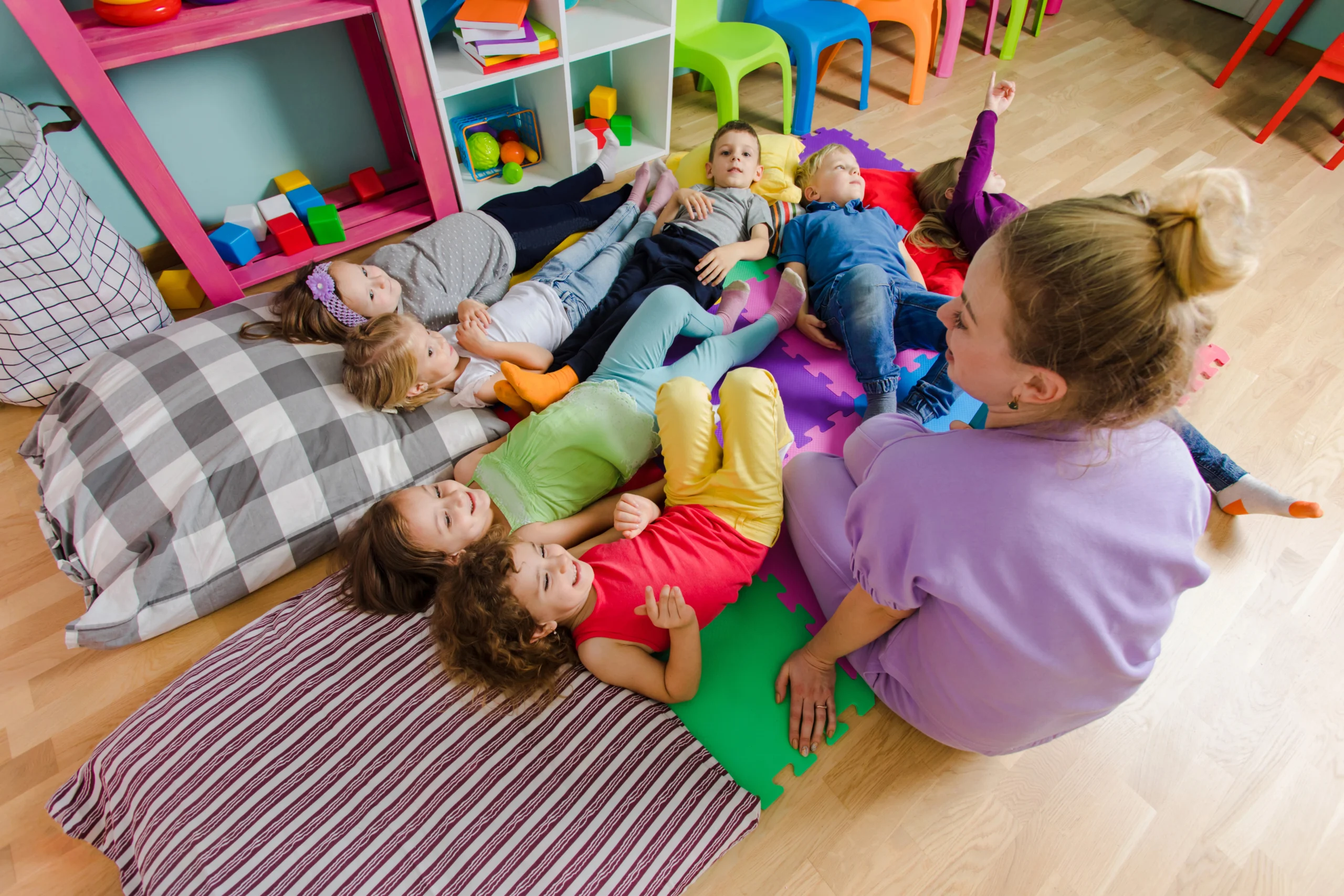 Kids laying on cushions in front of their preschool teacher.