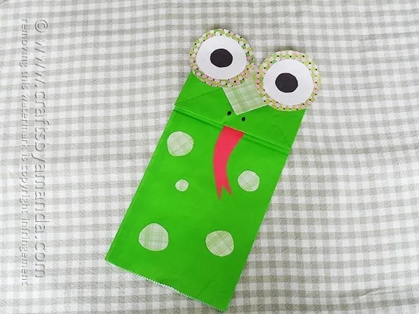 A paper bag frog puppet with it's tongue sticking out.