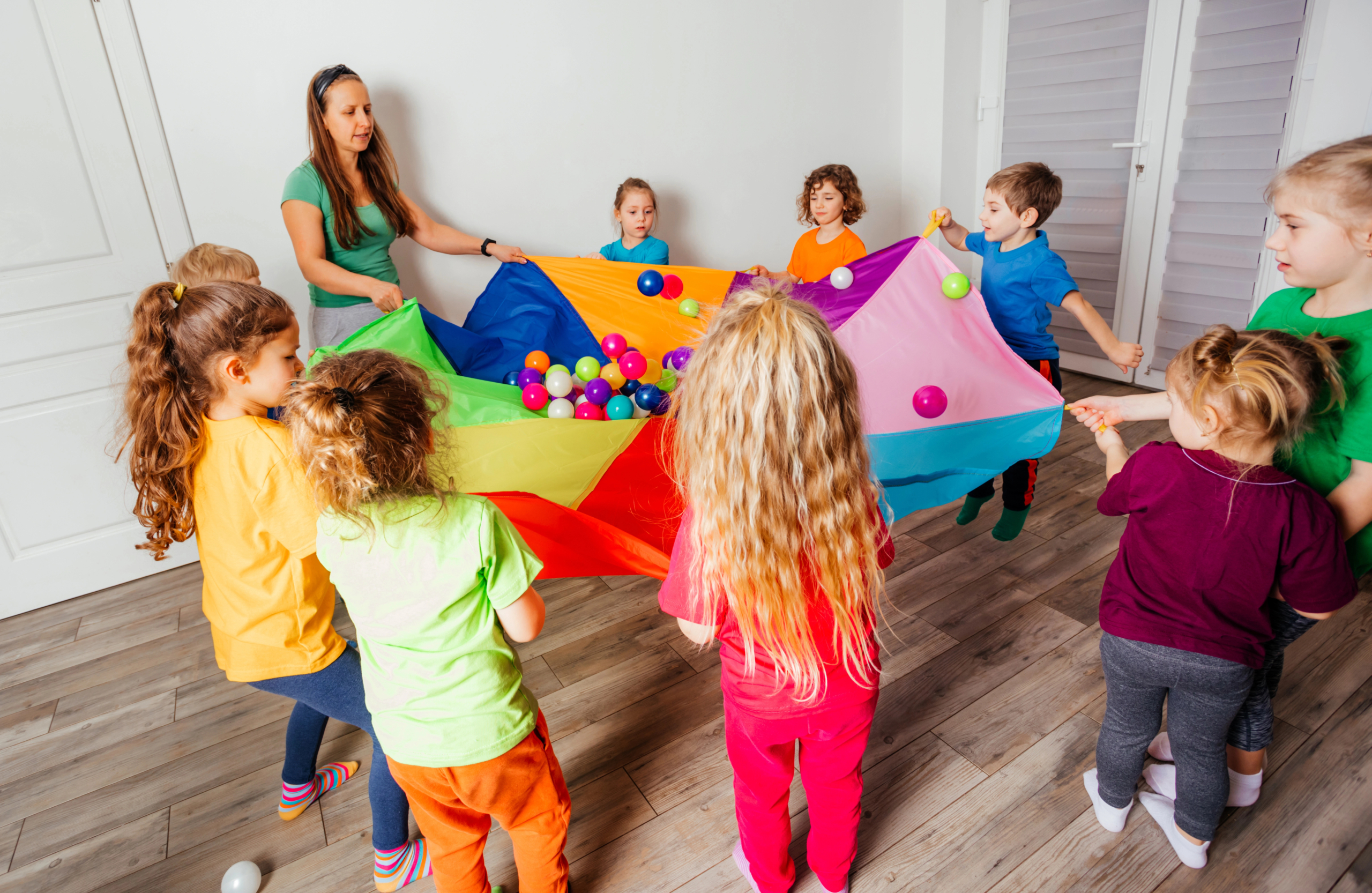 Kids in a circle holding a parachute with plastic balls on it.