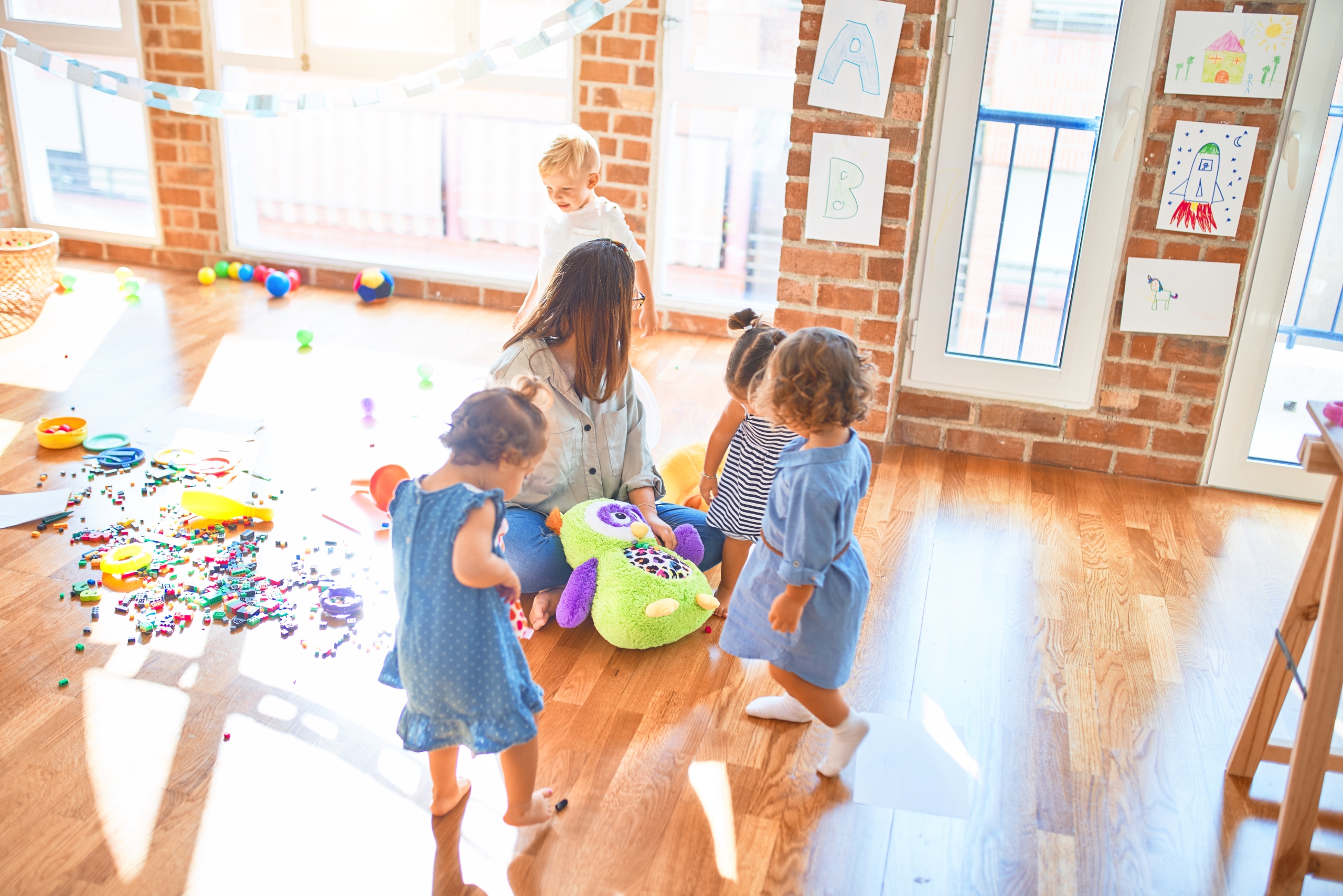 Kids in a preschool playroom with toys on the floor.