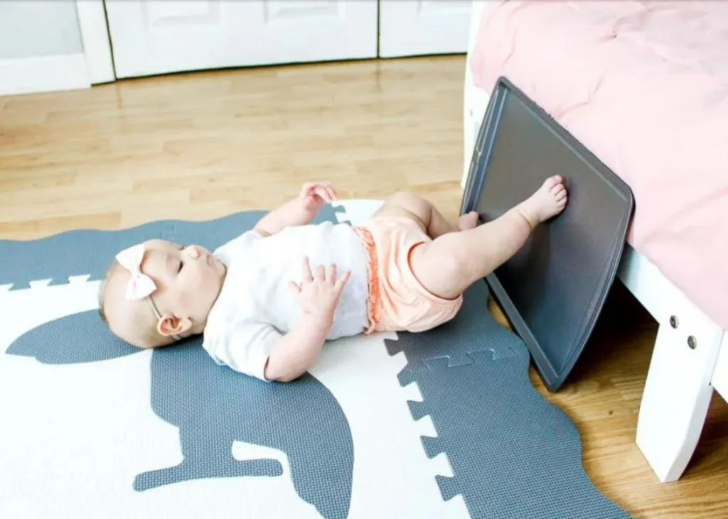 Baby taps feet on cooking sheet for sensory play.