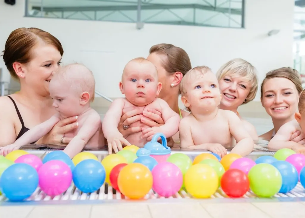 Moms hold their babies in a pool for swim class.