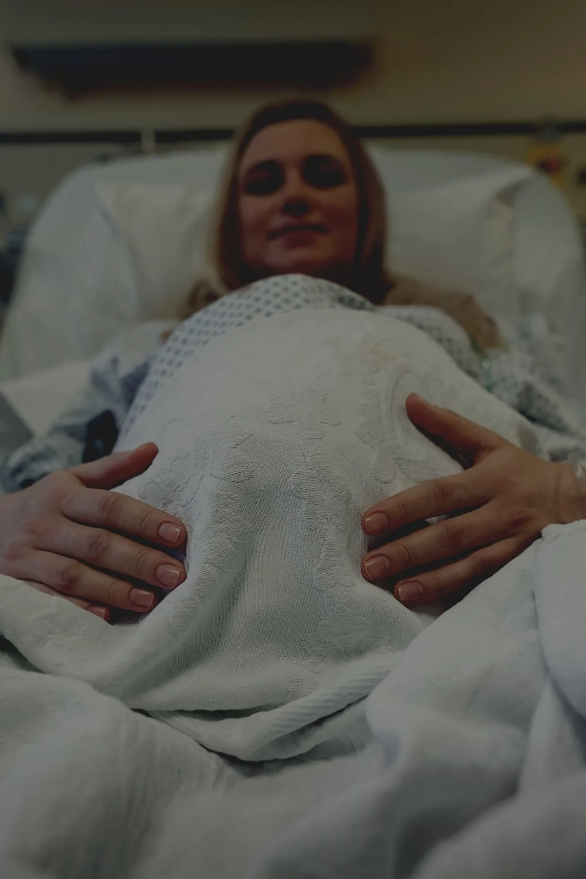 Pregnant woman prepares for birth on hospital bed in dimmed delivery room.