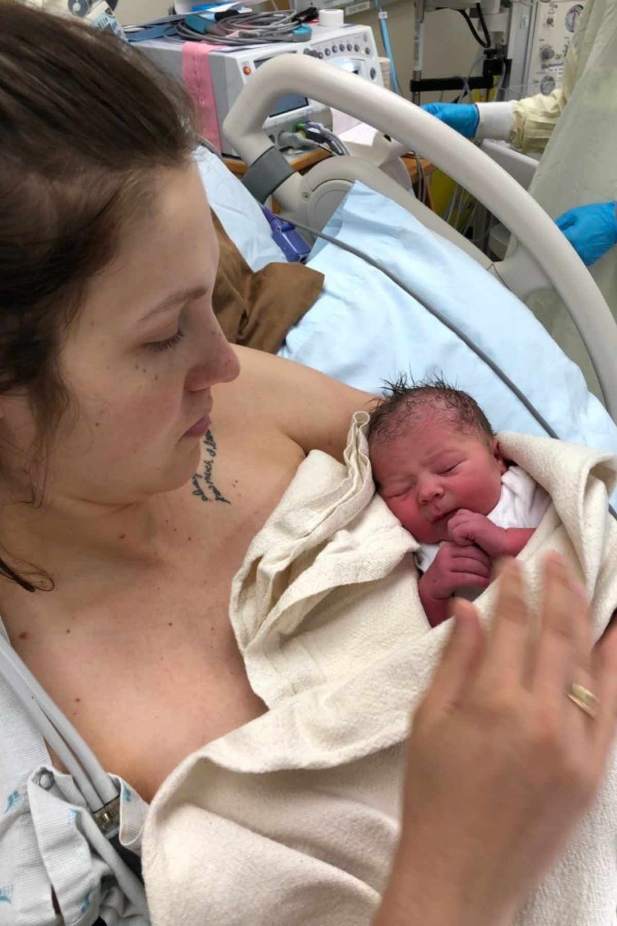 Mother holds her newborn baby in a hospital bed with a blanket.