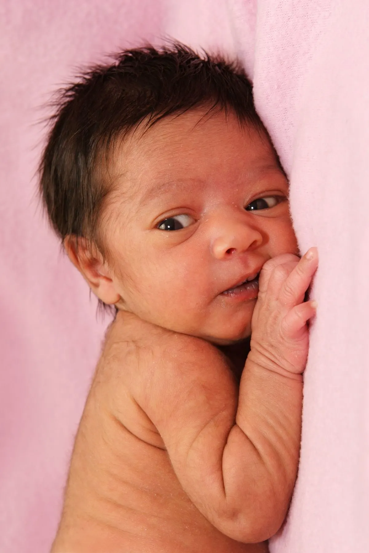 Baby with lanugo on back and shoulders lies in front of pink backdrop.