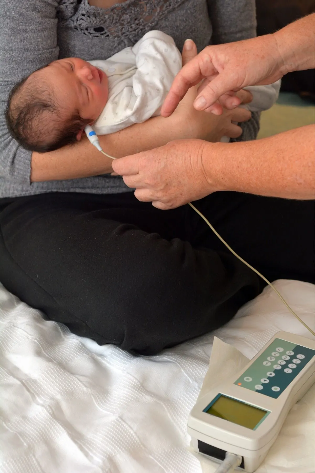 Mother holds newborn as he receives a hearing screening in the hospital.