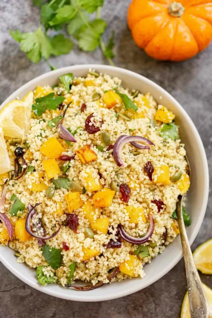 Pumpkin couscous salad with red onions and green garnish in a large bowl.