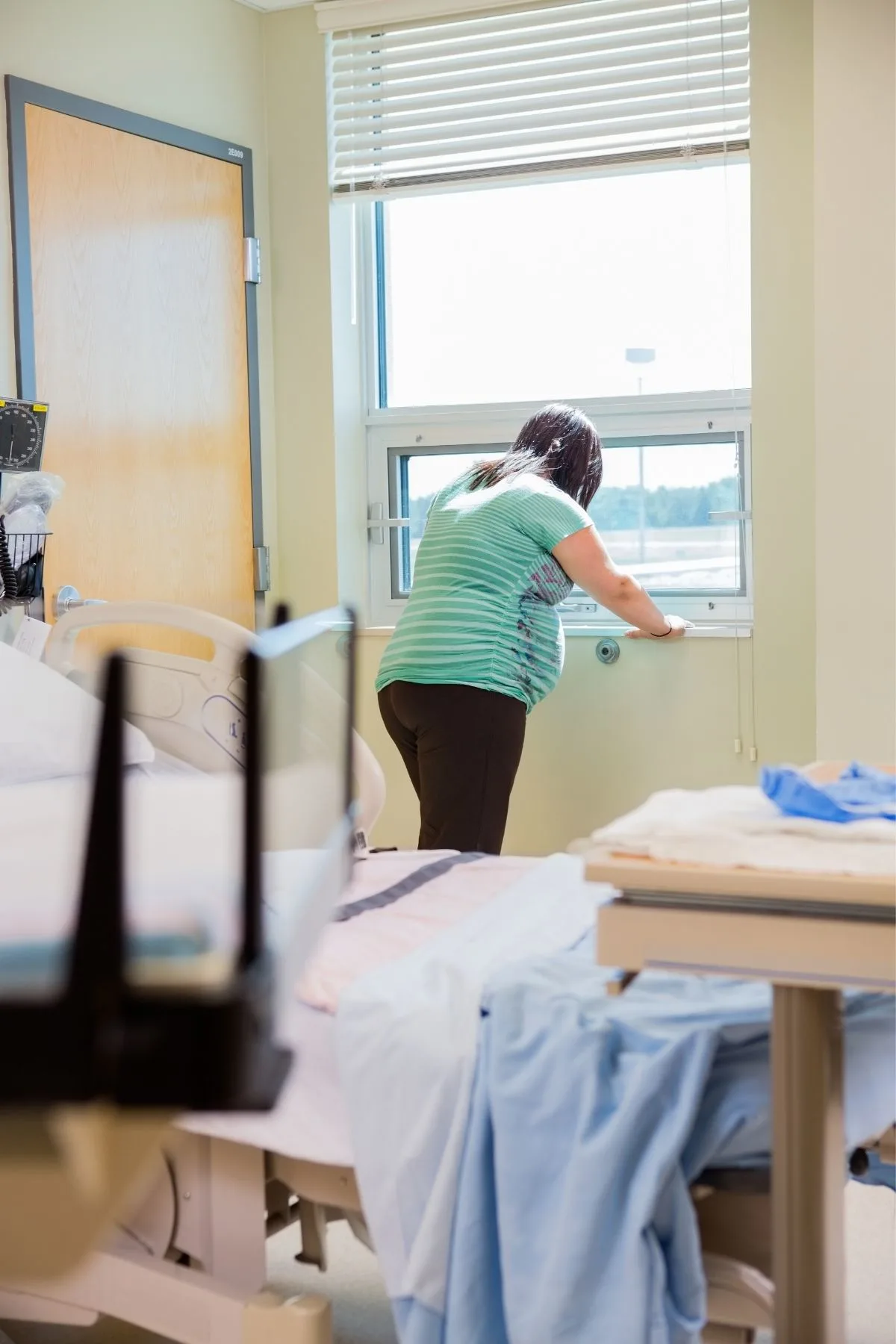 Woman stands in front of hospital window during birth to ease labor pains.