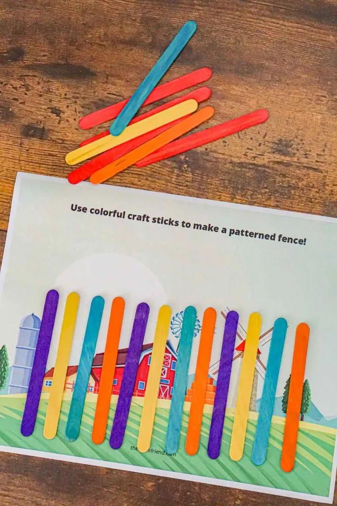 A "fence" made from craft sticks on a piece of paper with a picture of a barn to teach preschoolers about patterns.