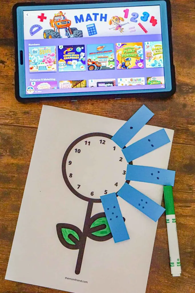 Preschool math activity where you stick on numbers to a paper clock with a tablet in the background. 